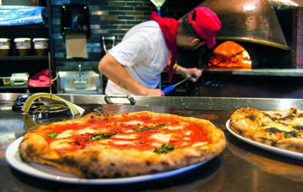Кухар ставить випікатися піцу в одному із закладів Неаполя. У більшості кафе цю страву готують за власними рецептами